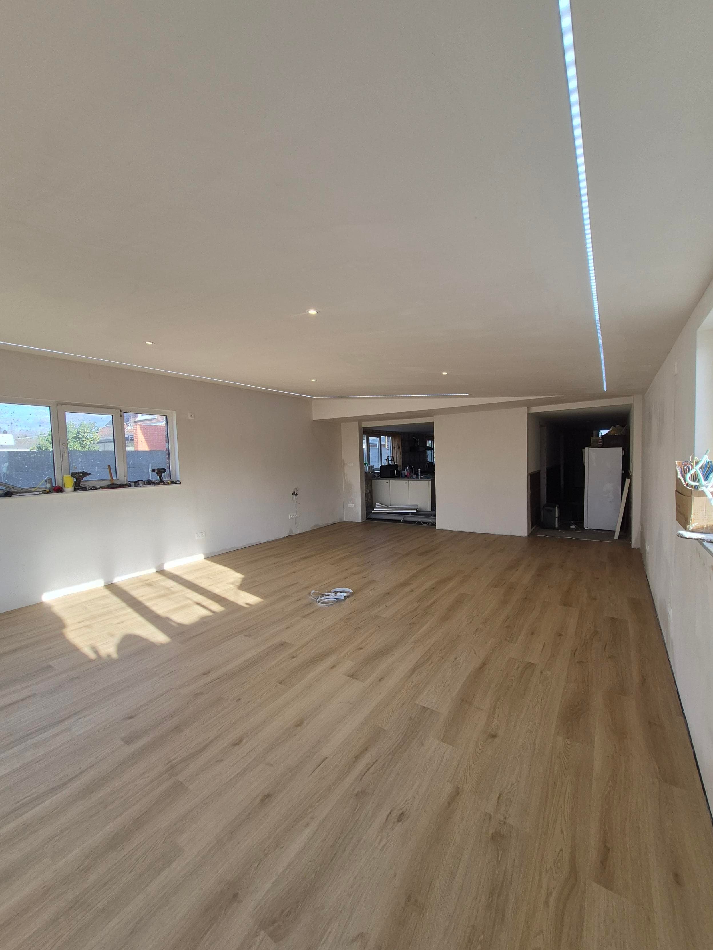 Empty room with light wood floors, white walls, and a long recessed LED ceiling light.