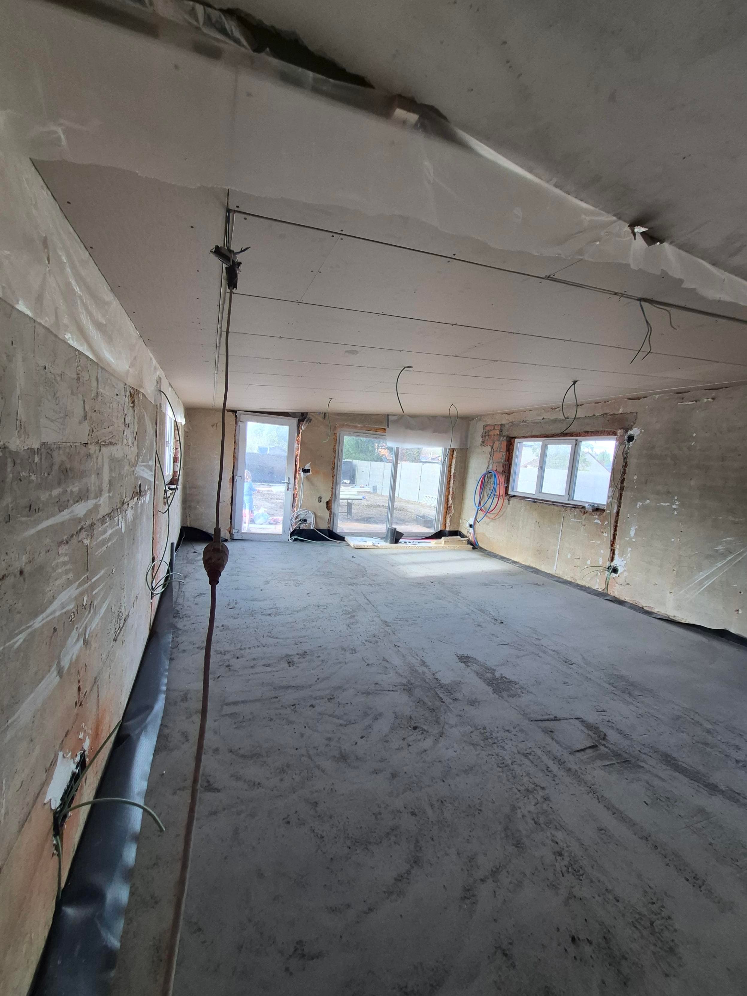 Unfinished interior room under renovation with concrete floor, plasterboard ceiling, and exposed electrical wiring.