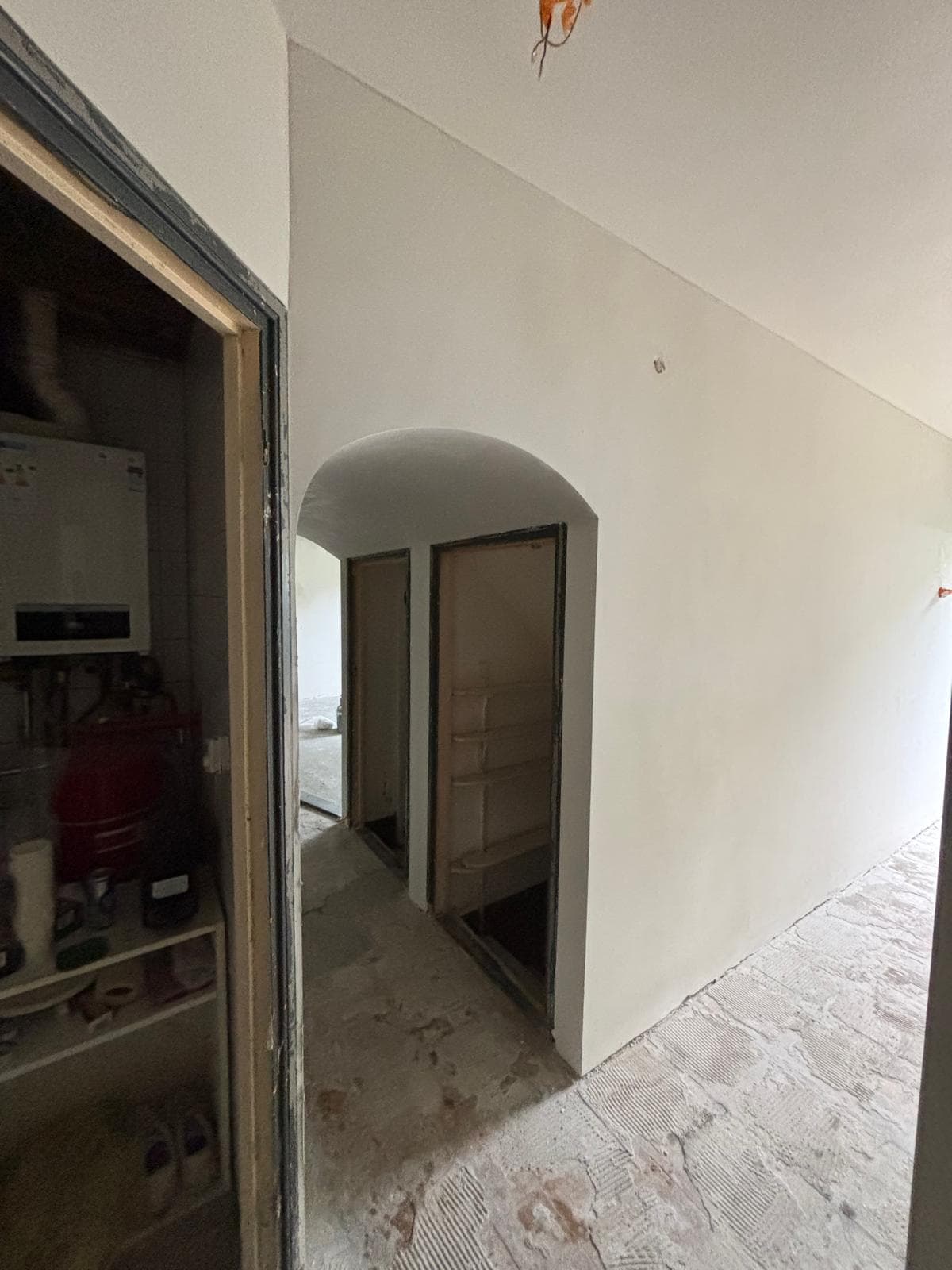 White interior hallway under renovation with an arched doorway and unfinished concrete flooring.